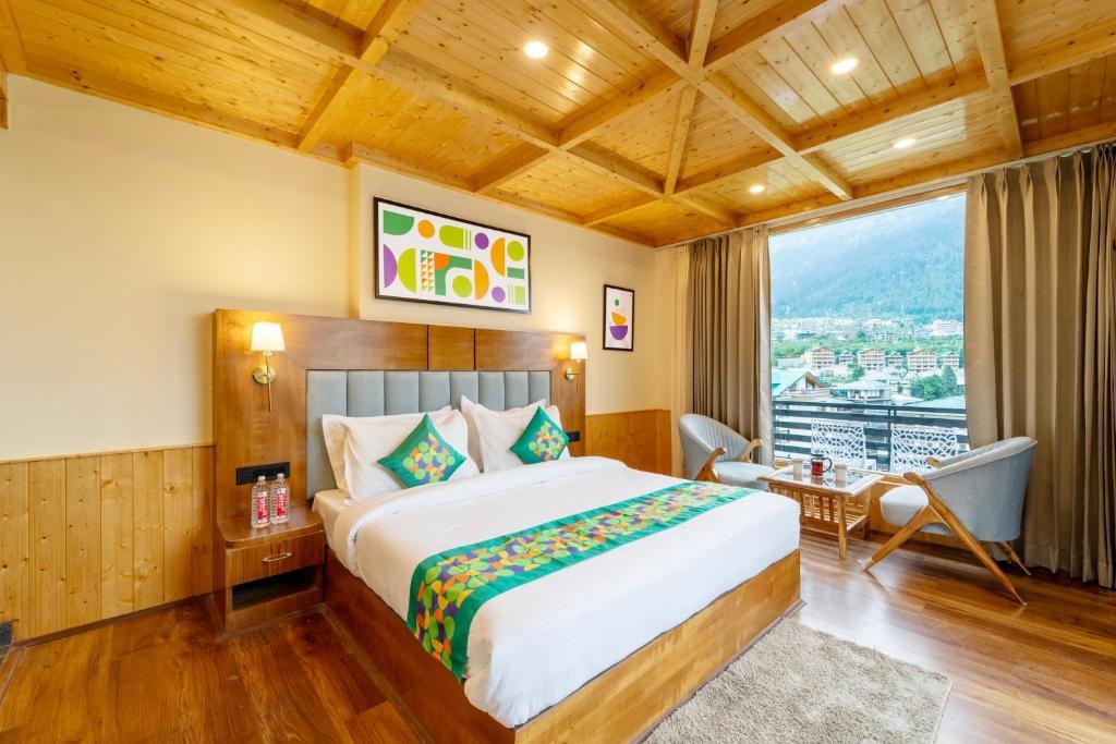 A modern hotel room with clean wooden decor, colorful pillows, and a large window view of the town.