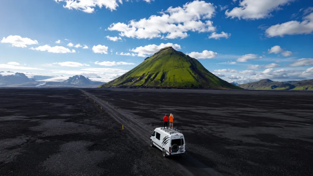 Camper van parked on Iceland's black sand plains with a green volcanic mountain in the background.